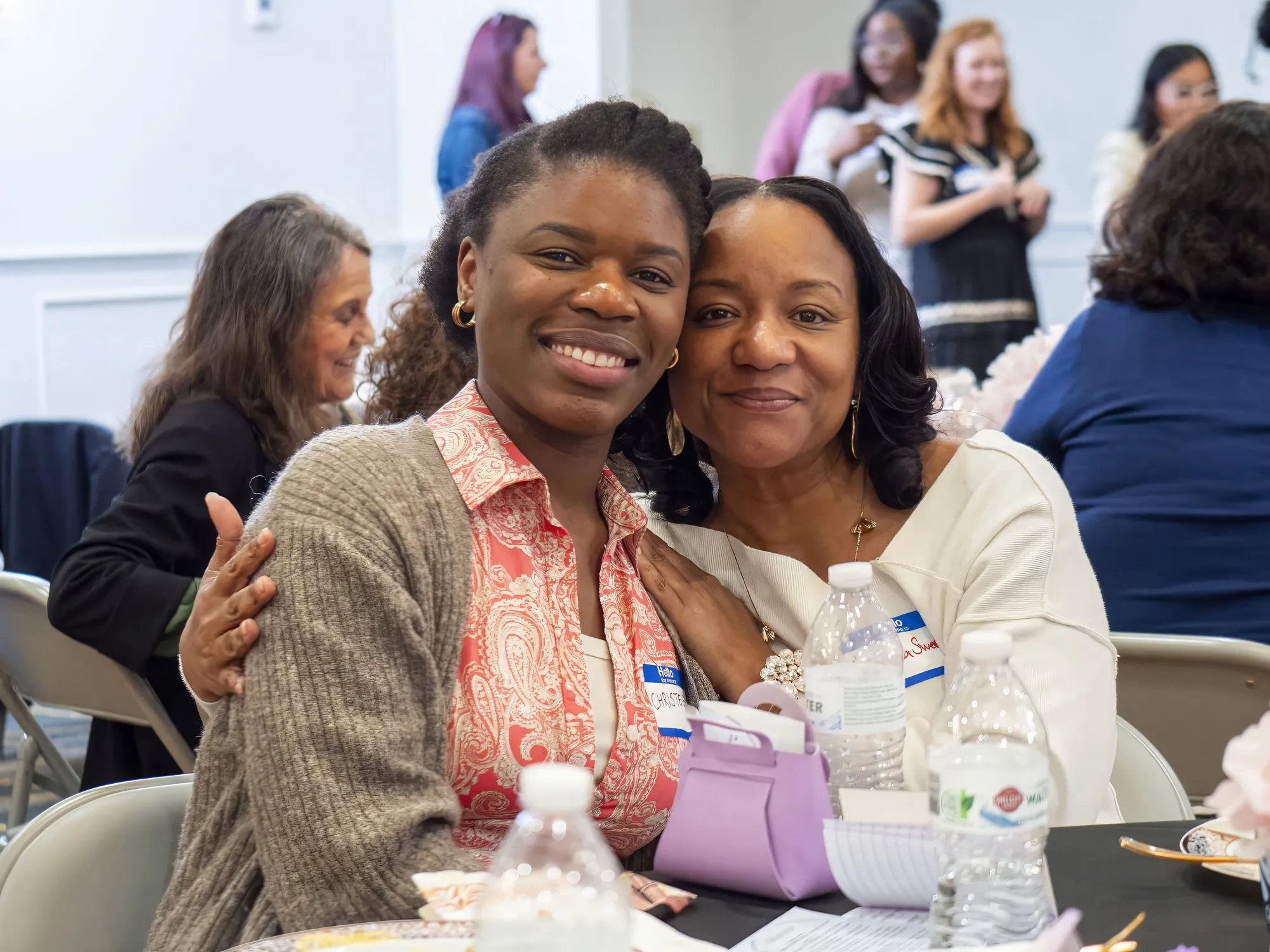Two women smiling cheek to cheek at their table
