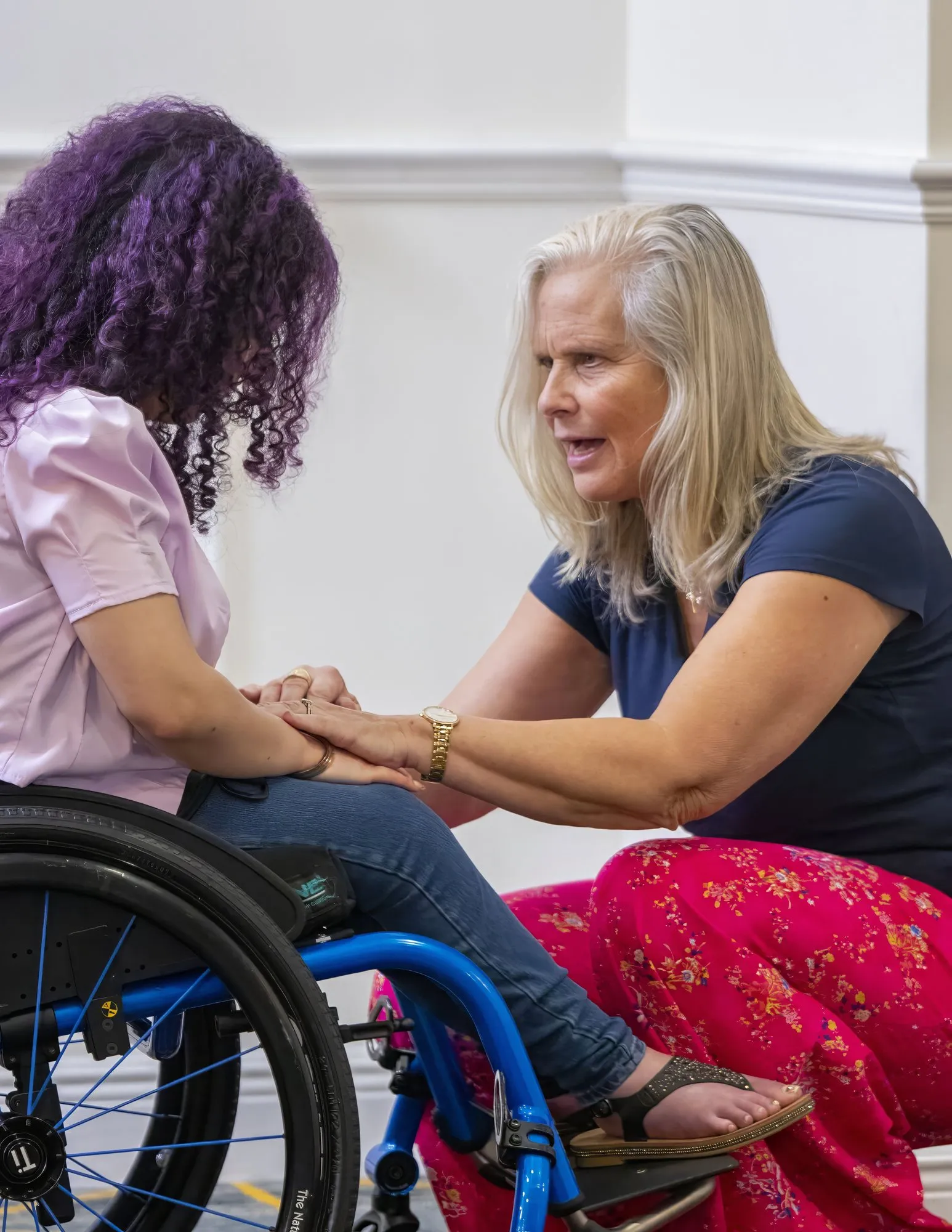 A woman kneeling to pray with a woman in a wheelchair