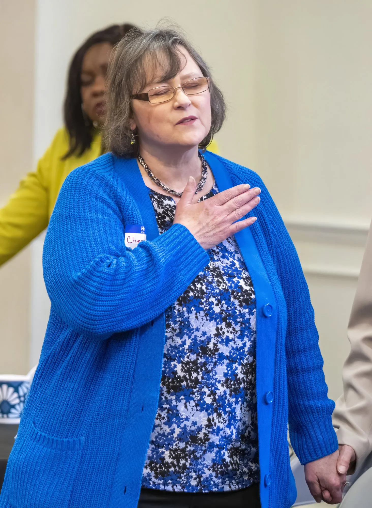 A woman standing in worship with her hand on her heart